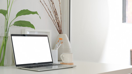 Cropped shot of minimal workspace with blank screen laptop, coffee cup and ceramic decorations