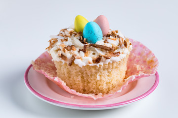 Easter cupcake made with toasted shredded coconut to create a nest for three little eggs, ready for eating.