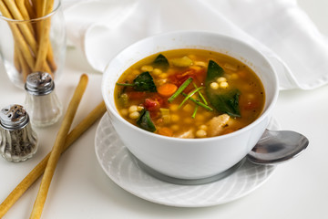 Top down view of a bowl of homemade chicken vegetable soup with breadsticks.