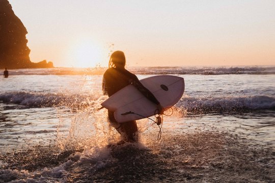 Young woman running out to sea with surfboard at sunset