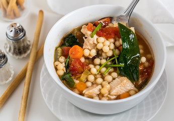 A top down view of a bowl of homemade chicken vegetable and pearl couscous soup ready for eating.