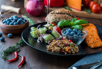 Close up view of a Mediterranean diet cuisine with foods including salmon, seven grain and greek salad and blueberries.