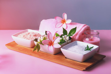 Obraz na płótnie Canvas Spa composition with bowls with rock white and pink salt and flowers, towel and candle. Body scrub and massage treatment
