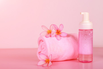 Fototapeta na wymiar Spa composition with towel, flowers and bottle of soap on pink background.