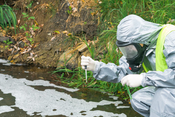 a man in a protective suit and mask conducts an express test of contaminated water to identify the level of danger to the environmental environment and living organisms