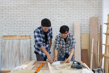 Two young asian carpenters pointing and writing on notebook in workplace - Handyman and diy concept