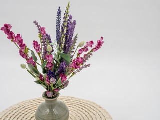 Purple and Pink Artificial Wildflowers in a Gray Ceramic Vase and an Off White Round Placemat.