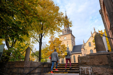 Two people are walking up the stairs to the Oslo Cathedral, located in the center of Oslo, Norway. In autumn, the leaves turn yellow and orange. - obrazy, fototapety, plakaty