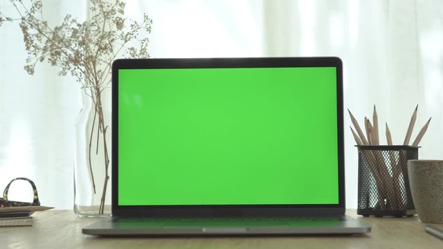 A computer laptop with green screen on the wooden table in home office