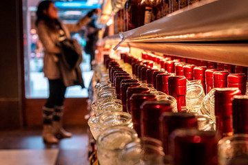 Perspective view of a bokeh of a woman shopping for wine or other alcohol in a liquor store standing in front of shelves full of bottles.