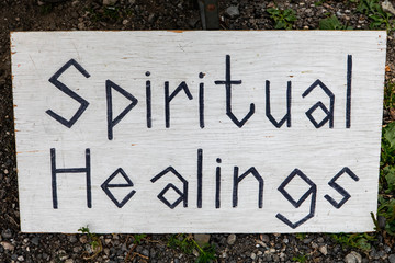 Hand written sign resting on an easel at the local farmer's market. Sign informs of spiritual healing practice. Black letters on white background.