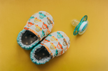 soft slippers made of cotton and ecological fabrics for a very small newborn with blue pacifier on...