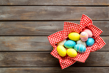 Basket with painted eggs for Easter dinner on dark wooden desk top-down copy space