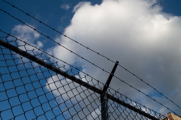 barbed wire silhouette fence with blue sky and white clouds