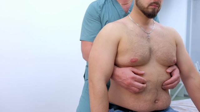Chiropractor treats patient's abdomen in clinic on rehabilitation therapy. Man on manual therapist appointment on treatment. Doctor palpates patient's under ribs. Checks operation of diaphragm.
