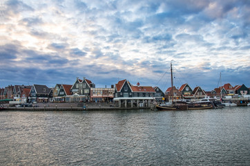 Fishing boats and yachts moored in marina in front of the traditional dutch wooden fishing houses in Volendam, Netherlands. Blue sky with heavy clouds.