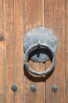 Old brown wooden massive gate, closed door, double entrance with handmade iron handles and knockers