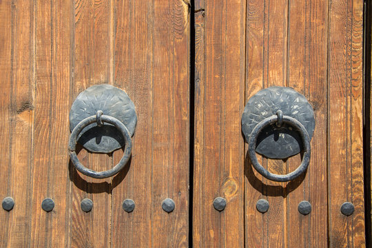 Old brown wooden massive gate, closed door, double entrance with handmade iron handles and knockers