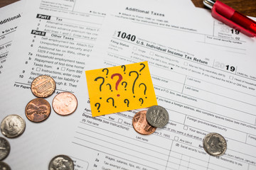 The pen, coins and sticker with question marks on the blank USA tax form 1040. Individual Income Tax Return. The time to pay taxes