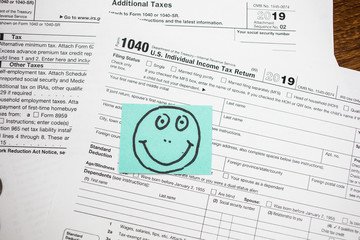 IRS 1040 tax return form with smiley face drawn on a sticker. Wage and tax statement concept