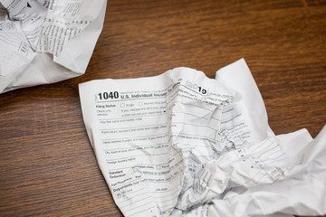 USA IRS tax form 1040 crumpled on a wooden table. Concept for frustration, difficulty and needing help in understanding tax laws and regulations