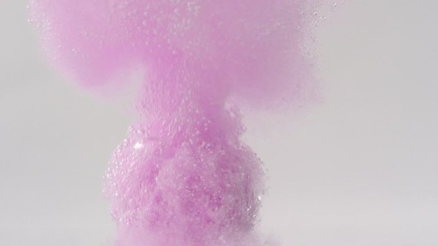 Underwater view of pink bath bomb falling down into clean water and exploding in slow motion against white background