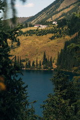Fototapeta premium Kazakhstan, Kolsalsky lake. Mountain lake among pine forests in the evening light Kazakhstan, Kolsalsky lake. Lake in the mountains among pine forests in the evening light. On a hill stand at home