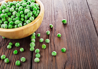 Bowl of frozen pea on a old wooden table.