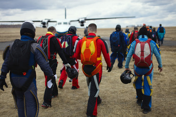 Team of skydivers with parachutes is walking to the plane before take-off, rear view, close-up.