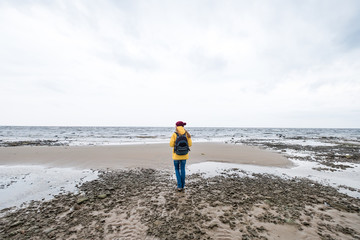 St. Petersburg. Russia Gulf of Finland. October. A girl with a backpack behind him in a yellow jacket stands and looks at the sea in cloudy weather.