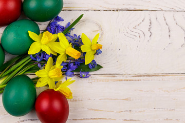 Painted Easter eggs and bouquet of yellow daffodils and blue scilla flowers on white wooden background. Easter composition. Top view, copy space