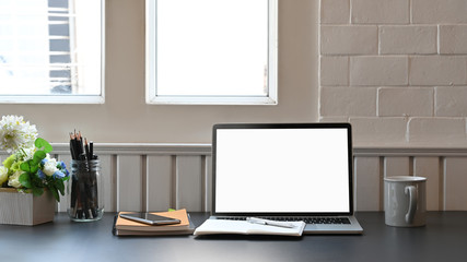 Photo of white blank screen laptop putting on the modern working desk including potted plant, coffee cup, notebook, pencil holder and smartphone. Comfortable workplace concept.