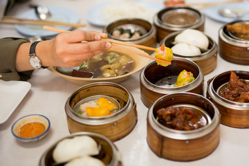 Hand holding chopsticks with steamed dumplings dim sum food in restaurant.