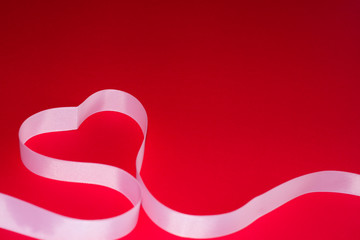 heart made of pink ribbon on a red background. the concept of holidays such as Valentine's Day, women's day, March 8, birthday. for postcards. the view from the top. space for text.
