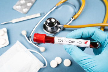Doctor holds a test tube with blood in his hand. A positive blood test for a new coronavirus. Against the background of the doctor’s workplace
