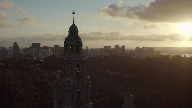 Aerial drone footage of the iconic buildings and towers of Balboa Park during a beautiful Sunset with the San Diego, California skyline is the background. 