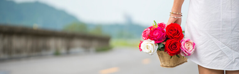 A beautiful woman wearing a white dress shirt standing, her carrying a basket of flowers-panoramic banner for web header
