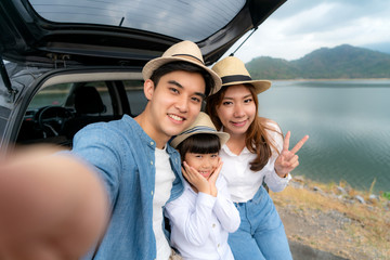 Portrait of Asian family sitting in car with father, mother and daughter selfie with lake and...