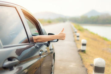 Hand of man traveler with thumbs up from car form the asphalt road go to travel with beautiful landscape lake and mountains and sunlight in evening. Copy space on right side.