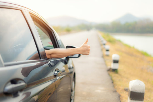 Hand of man traveler with thumbs up from car form the asphalt road go to travel with beautiful landscape lake and mountains and sunlight in evening. Copy space on right side. - Powered by Adobe