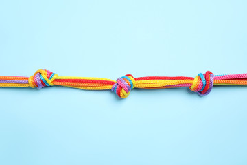 Colorful ropes tied together on light blue background, top view. Unity concept