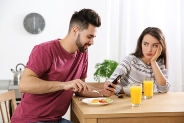 Young man preferring smartphone over his girlfriend at home