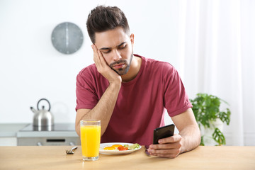 Fototapeta na wymiar Young man addicted to smartphone having breakfast at home