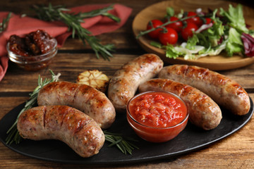 Tasty grilled sausages served with sauce on wooden table