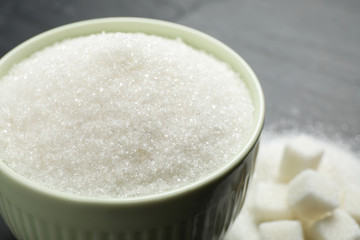Granulated sugar in bowl on dark grey table, closeup