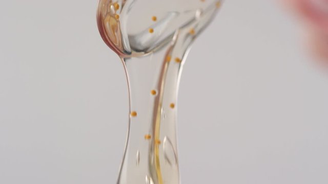 Sequence of shots of female hand holding applicator with gold jelly essence flowing down into container against white background