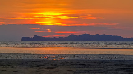 view panorama seaside evening of sand beach with mountain and red sun light in cloudy sky background, sunset at Chao Mai Beach, Had Chao Mai National Park, Trang Province, southern of Thailand.