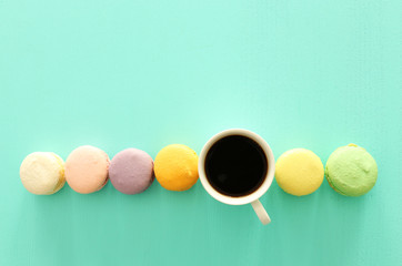 White cup of coffee and colorful macaron or macaroon over pastel wooden table
