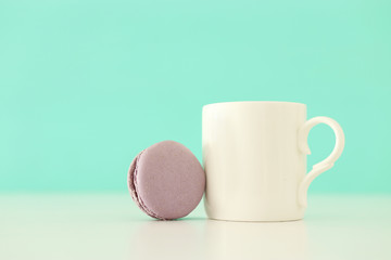 White cup of coffee and colorful macaron or macaroon over pastel wooden table