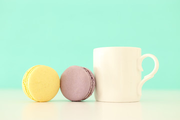 White cup of coffee and colorful macaron or macaroon over pastel wooden table